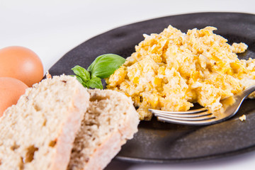 Scrambled eggs, some fresh eggs and wholemeal bread, and a fork, decorated with basil, on a white background 