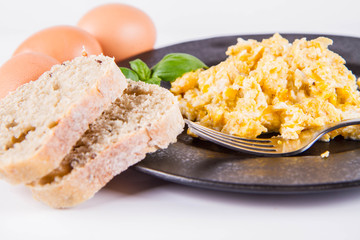 Scrambled eggs, some fresh eggs and wholemeal bread, and a fork, decorated with basil, on a white background 