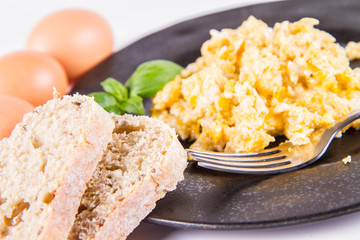 Scrambled eggs, some fresh eggs and wholemeal bread, and a fork, decorated with basil, on a white background 