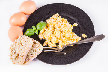 Scrambled eggs, some fresh eggs and wholemeal bread, and a fork, decorated with basil, on a white background 