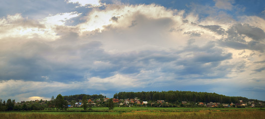 Picturesque rural landscape. Scenic sky with clouds, houses and trees. Panoramic shot.