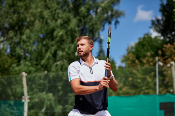 Determined blonde male tennis player is ready to return a strong serve, being motivated by a trainer to a win.