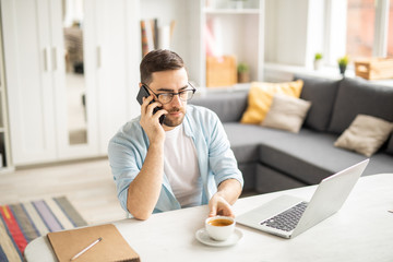 Serious businessman with smartphone going to have a cup of coffee while calling client or colleague by workplace