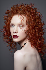Fototapeta premium Beautiful young woman with red-hair on grey background. Nude pretty lady with bright red lipsstick and modern art makeup. Sensual model pose in photo-studio. Sexy naked body.