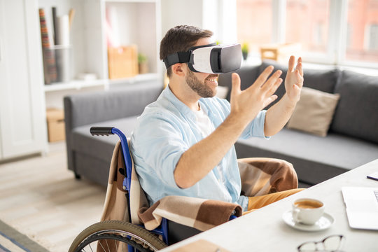 Cheerful young casual businessman in vr goggle keeping his hands in front of himself while looking at something virtual