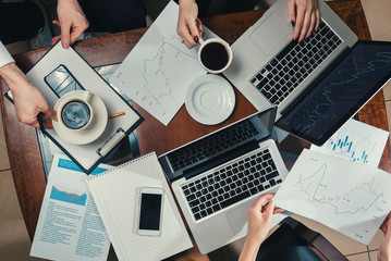 Team work/ Workplace with laptop, documents, notepad, sheet of paper, coffee, mobile, currency graphics, hands of employees