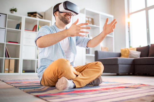 Happy young casual man with vr headset holding virtual stuff in hands while interacting in virtual reality