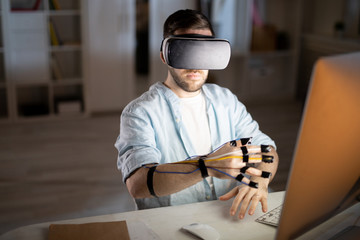 Businessman in vr headset keeping his hand with sensors on fingers by computer screen while traveling in virtual world