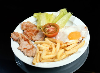 Plato con dos cortes de lomo a la parrilla, un huevo frito, ensalada y patatas fritas.