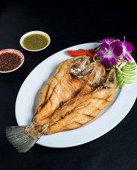 fried fish with souce on white plate black background