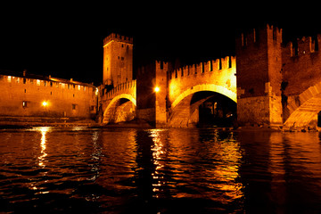 Fototapeta na wymiar Castelvecchio bridge in Verona taken from the river during a winter evening illuminated by vintage lights