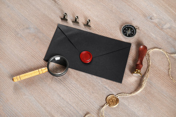 Blank black vintage envelope, sealing wax, magnifier, stamp, compass and stamp on wooden...