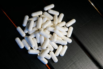 White pill capsules lie on a black wooden background with LED light.
