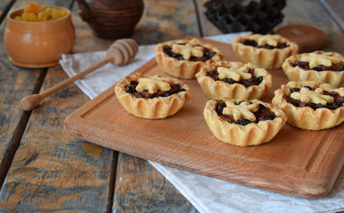 Mini Tartlets with dried fruits and nuts. Shortbread cookies with fruits stuffing on wooden background. Small sweet pie. Copy Space.