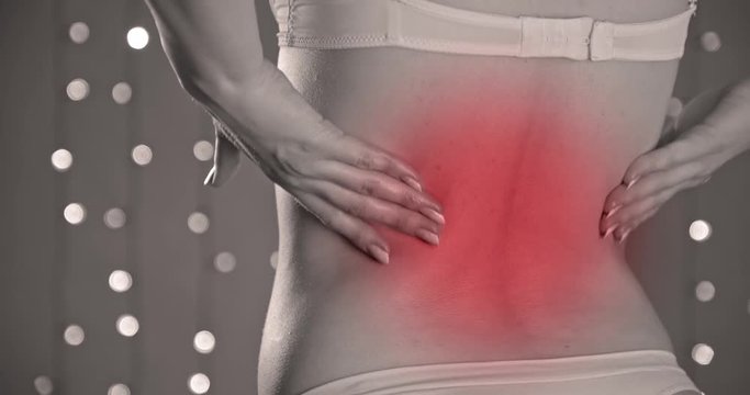 Pain concept. Closeup of a woman's back with backache  on a yellow background with lights