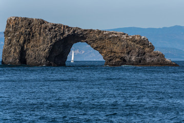 Small sailboat is visible through the Anacapa Island Arch on a sunny winter day in the Channel Islands National Park off the Pacific Ocean coast of Ventura.