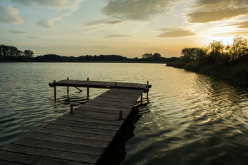 Wooden bridge with planks on the lake and clouds in the sky during sunset