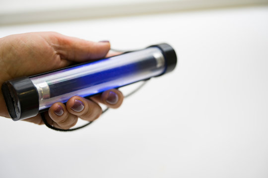 Hand holding a miniature UV lamp.  The lamp shines blue.  Selective focus. Copy space.