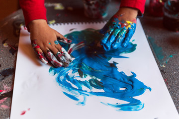 Playing with blue finger paint on white paper surface.