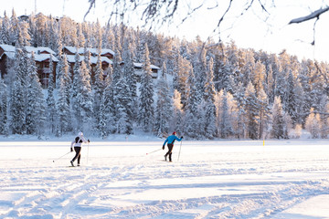 Skiers runners glide through the snow. Winter lake in Kuusamo Ruka. Finland. Mount c houses and trees, a springboard for jumps on skis.