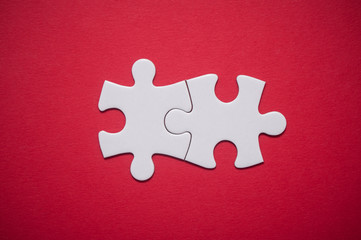 Closeup of two connected jigsaw puzzle pieces on red background. The concept of finding the right solutions in teamwork.