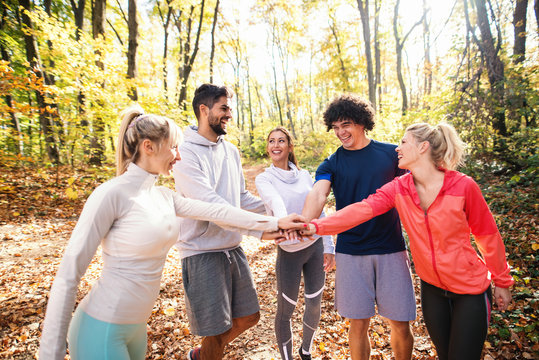 Happy group of runners smiling and stacking hands while standing in woods in autumn.