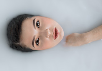 People, resort and recreation concept. Good looking natural young woman rests in milky aroma bath, resting in spa resort