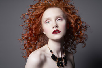 Beautiful young woman with black jewelry and red-hair on grey background. Nude pretty lady with...