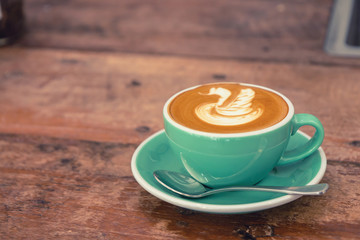Hot cappuccino coffee in a green cup with latte art on the wooden table in the coffee shop. Vintage colored tone.