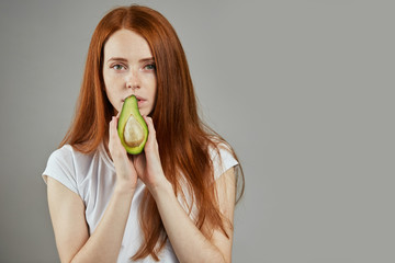 good looking woman is going to eat avocado. isolated grey background. copy space