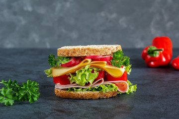 Graham bread sandwich with ham, cheese and fresh vegetables on a dark background. Breakfast concept.