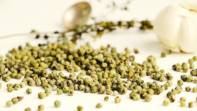 Green peppercorns - pepe verde - famous spice of italian cuisine on white table with garlic bulbs, thyme twig and spoon.