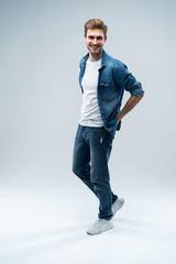 Modern and casual. Full length of handsome young man looking at camera with smile whilestanding against grey background.