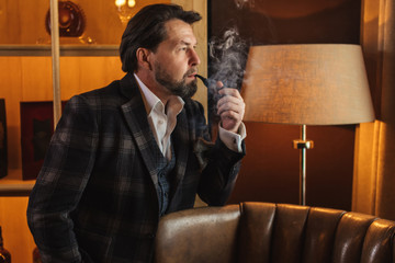 Anxious husband in a tweed jacket looking through the window, nervously puffing his pipe, worrying...