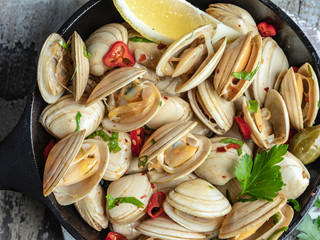 Cooked seafood clams in the iron pan portion with lemon and seasoning. close-up