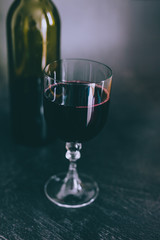 glass of intensely coloured red wine and bottle on dark background