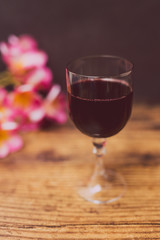 glass of intensely coloured red wine and tropical Australian flowers on wooden table