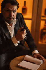 Mature businessman making notes while sitting at restaurant. Senior well-dressed caucasian man in age, enjoying rest time in tobacco pipe club.