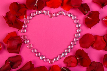 Heart of beads on a pink background decorated with rose petals.