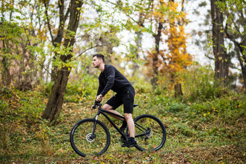 Fototapeta na wymiar Young handsome sport man with his bike training in park in autumn time, with colorful background