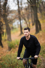Obraz premium Young pretty man standing with bicycle in colorful autumn park. Fall season background.