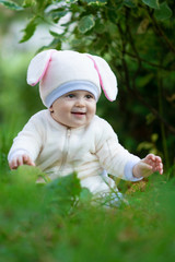 Child in bunny suit seating on grass in park.