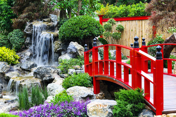 Fototapety  Czerwony most i sztuczny wodospad z drzewami i kolorowymi kwiatami w japońskim ogrodzie.