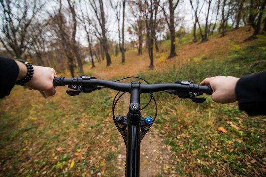 Close-up image of cyclist man hands on handlebar riding mountain bike on trail in autumn park