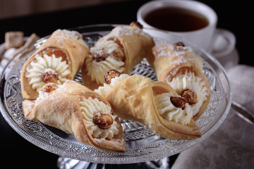 Delicious little cakes with cheese cream filling on a cake stand on a dark background next to the tea sets