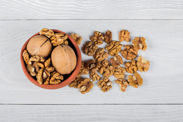 whole walnuts and kernels on a white wooden background, walnut on a light old table in a clay pot