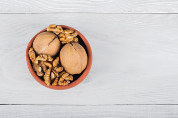 whole walnuts and kernels on a white wooden background, walnut on a light old table in a clay pot