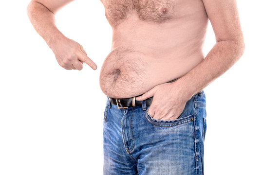 Young topless man points with forefinger to his fat stomach belly button islolated on white background - concept getting rid of belly fat, overweight, diet, lifestyle, health, weight loss or gain