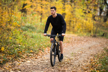 Naklejka premium Handsome man biker in cycling clothing training on bicycle, getting ready for race in park on fresh air. Man enjoying morning bike ride. Concept of motivation, healthy lifestyle