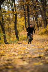 Fototapeta premium Young athlete ride with bicycle on the autumn park. Preparing for training